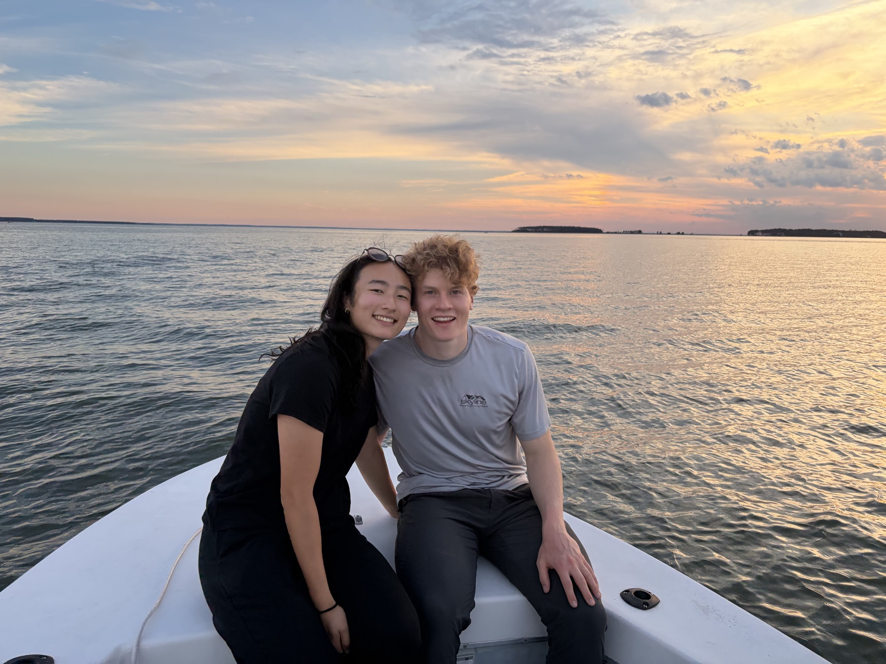 Sumi and Shane smiling together on the bow of a boat at sunset